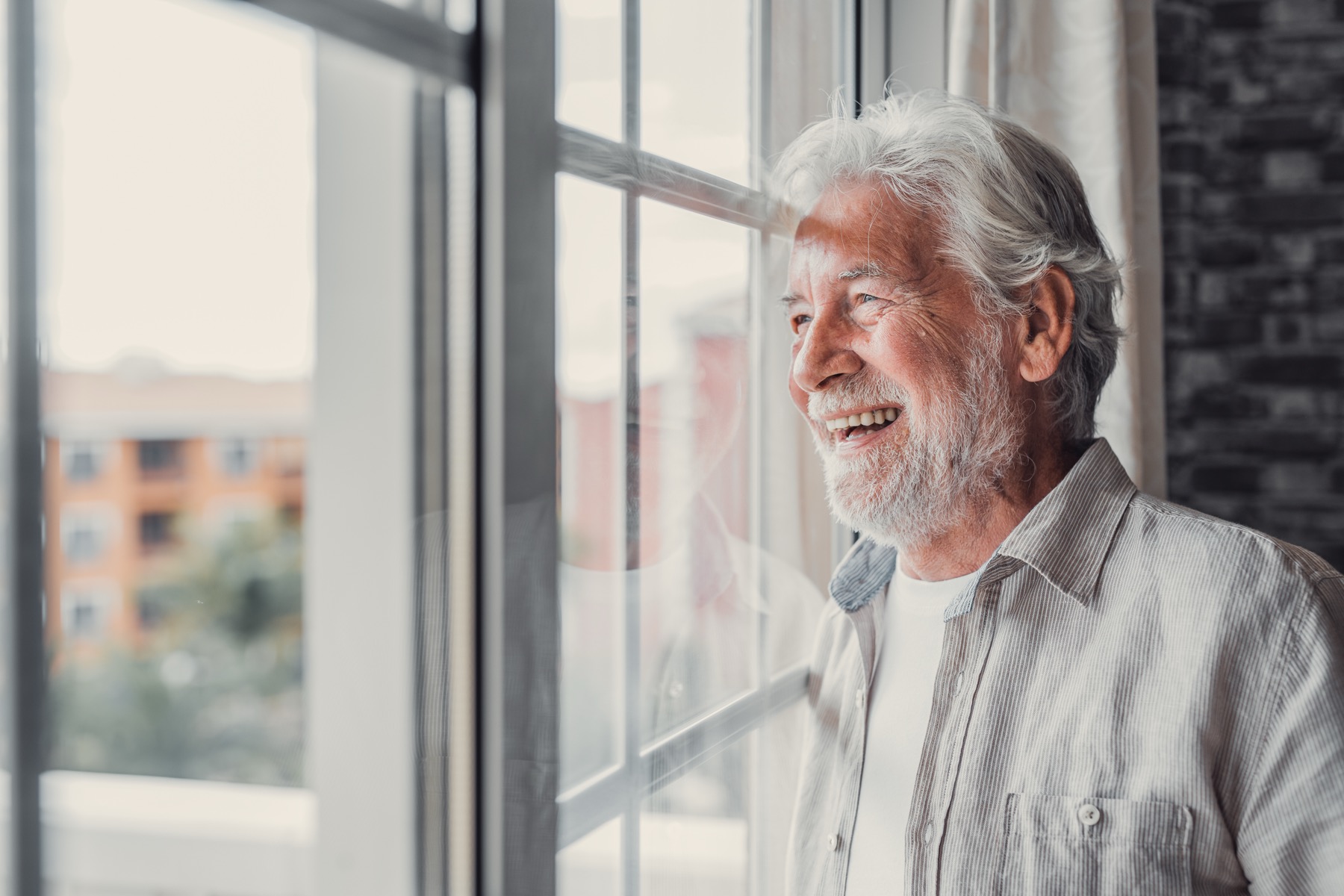 An older man at home looking out a sunlit window